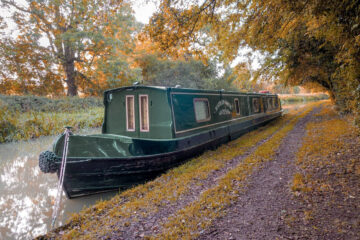 Luxury Boutique Narrowboat cruising a tranquil autumn canal with golden foliage