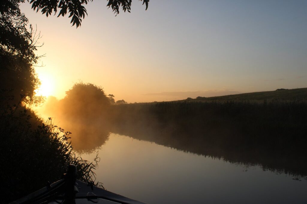 Luxury Boutique Narrowboat moored on a misty UK canal in autumn, surrounded by golden foliage and calm reflective waters