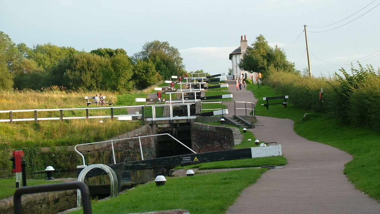 oxton Locks on the Grand Union Canal, featuring a flight of historic narrowboat locks surrounded by lush greenery and towpaths, with canal boats navigating the staircase.