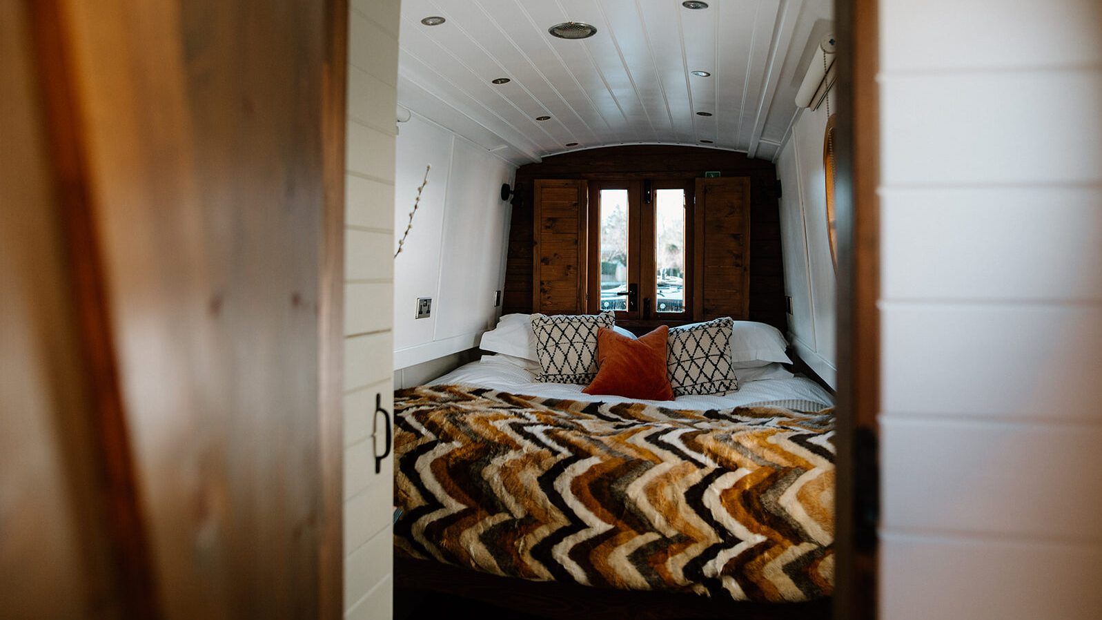 Cosy interior of a dog friendly narrowboat bedroom with warm lighting, wood panelling and patterned bedding.