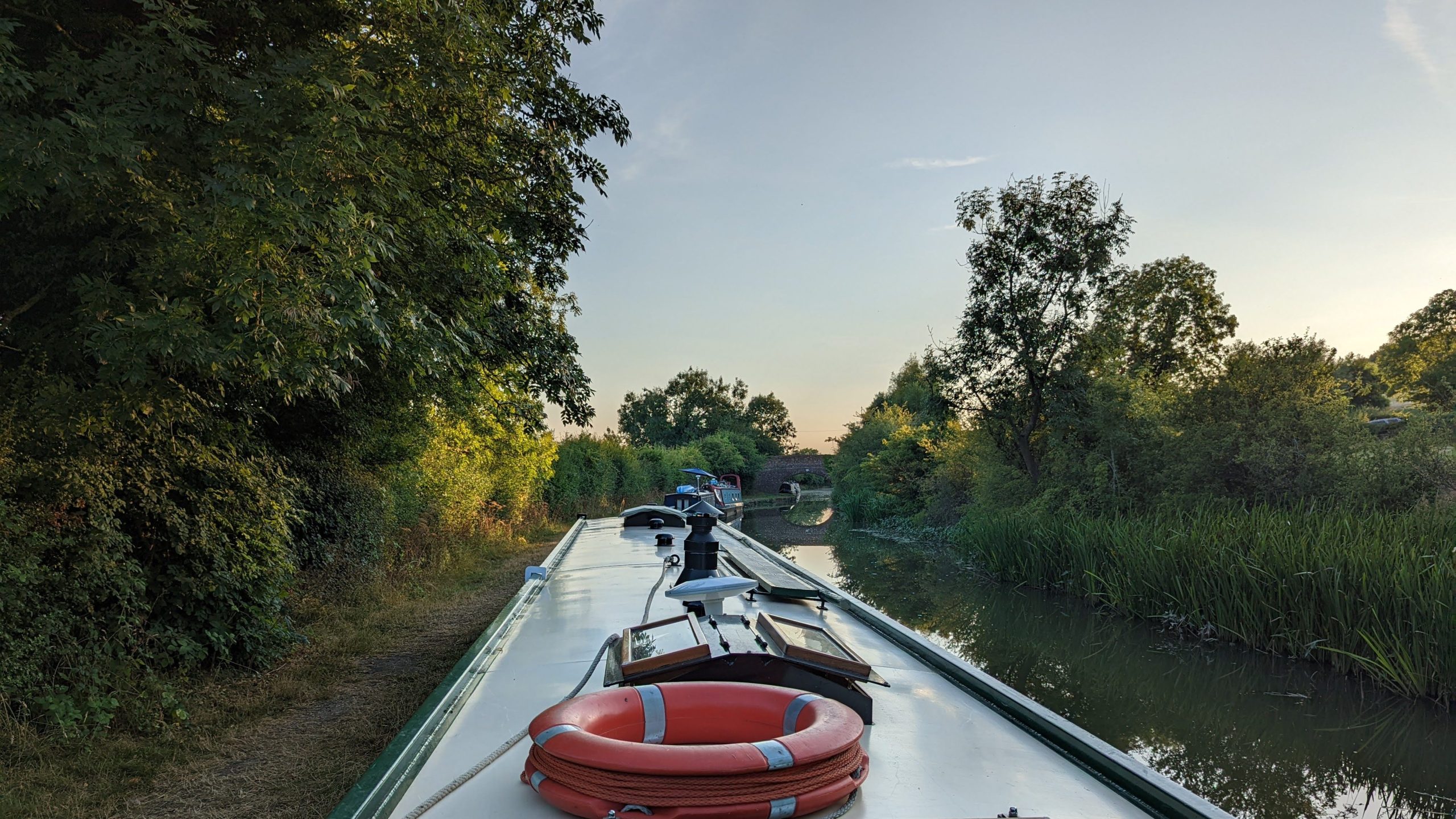 narrowboat cruising along a peaceful canal surrounded by green countryside at sunset