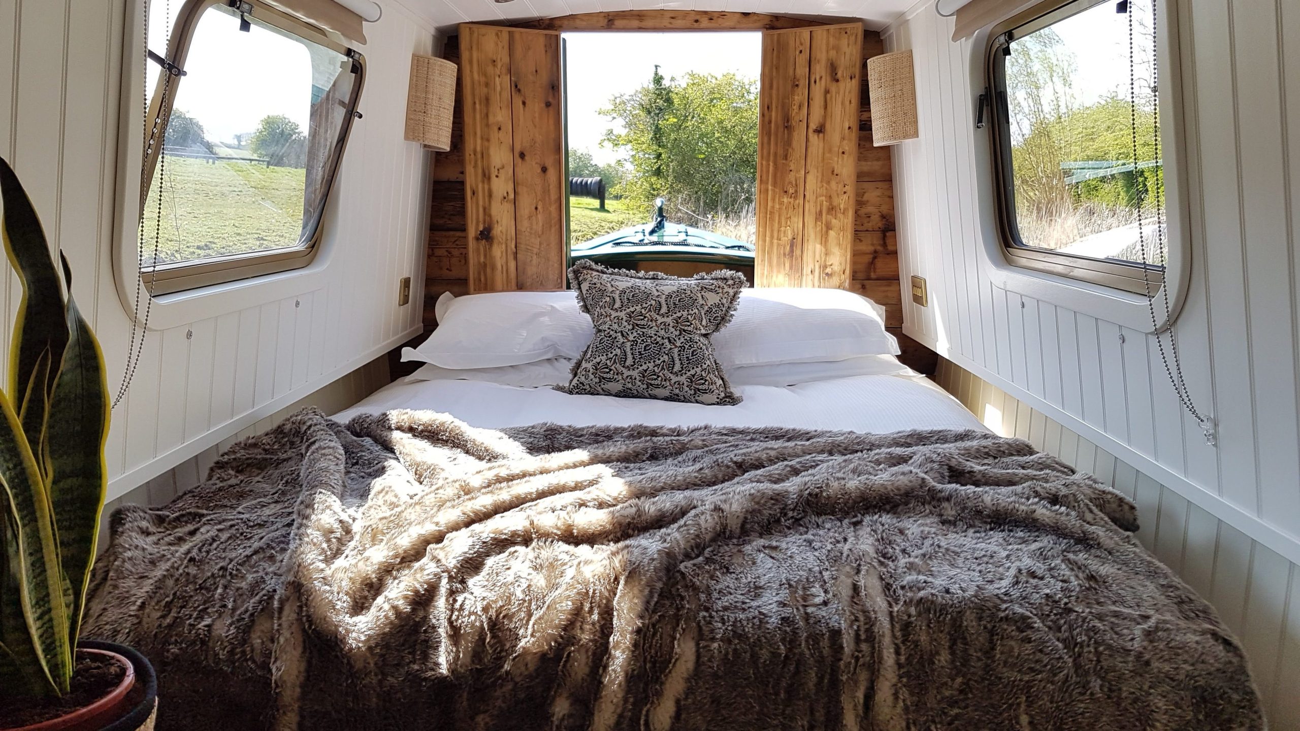 Cosy boutique narrowboat bed with soft blankets and a peaceful view through the bow doors.
