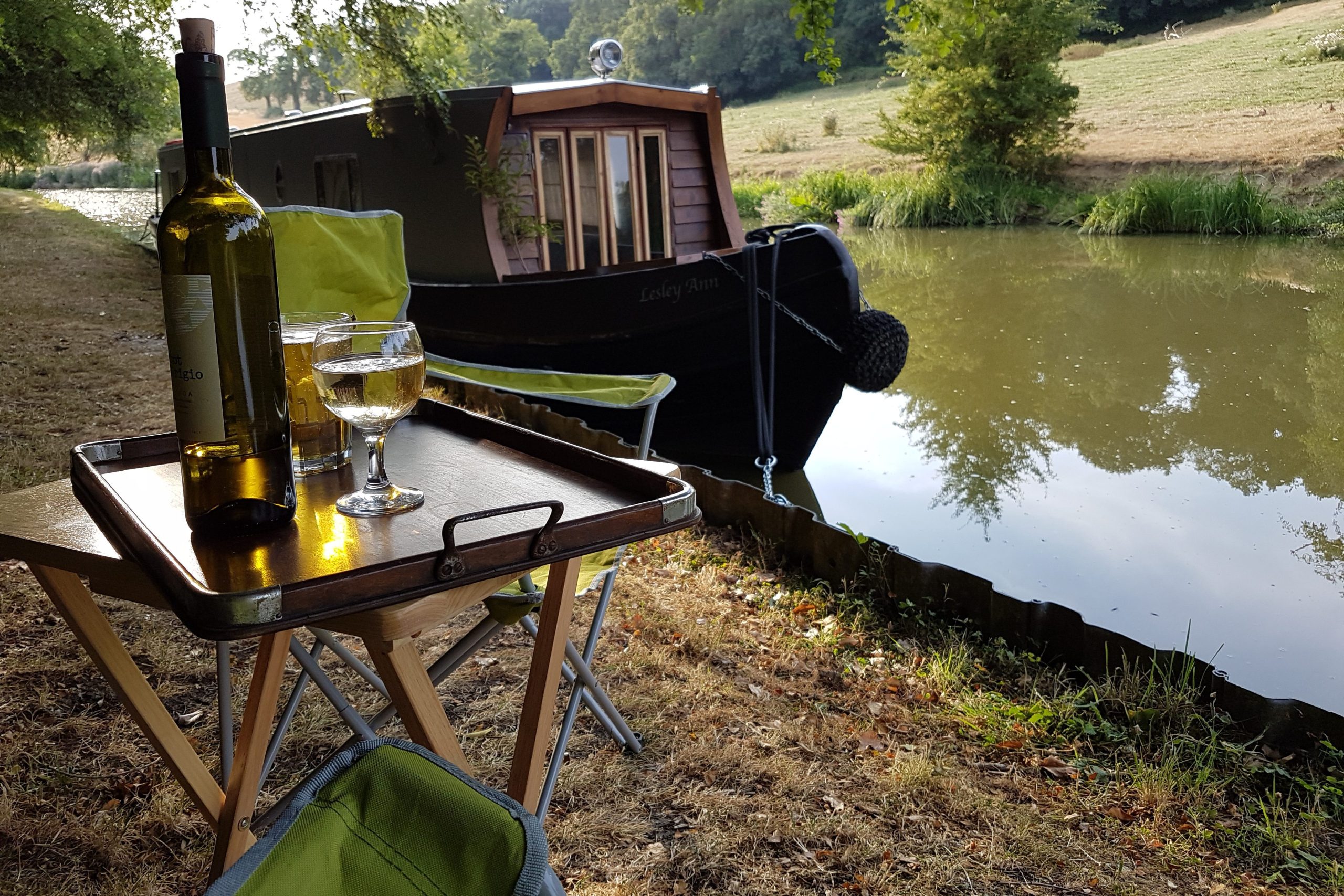 Luxury narrowboat holiday moored beside calm canal with drinks on deck