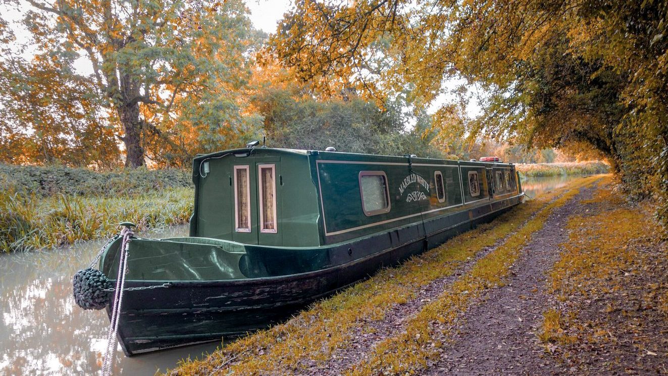 Luxury Boutique Narrowboat cruising a tranquil autumn canal with golden foliage